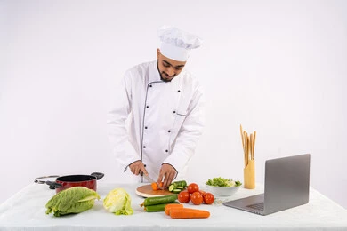تعلم فنون الطبخ في الدورات التدريبيه عبر الحاسب المحمول، بورتريه لرجل عربي خليجي اماراتي يرتدي زي العمل يقوم بتحضير وصفة طبق صحي مفيد من الانترنت، شيف سعودي يقوم بتقطيع الخضراوات الطازجة، استخدام المكونات والمقادير المناسبة للوجبة، خلفية بيضاء