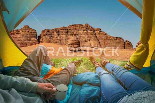 سائحان يجلسان داخل خيمة مطلة على التكوينات الصخرية في العلا في شمال غرب المملكة العربية السعودية ، جمال التكوينات الصخرية في السعودية ، معالم اثرية سياحية في السعودية ، رحلة سياحية