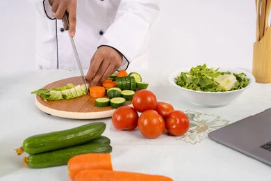 شغف التدرب على مهارة الطهي وإعداد الطعام، احترافية تقطيع الخضار، بورتريه مقرب لرجل عربي خليجي اماراتي يرتدي زي العمل يحضر طبق صحي مفيد، شيف سعودي يقوم بتحضير سلطة الخضراوات الطازجة، استخدام المكونات والمقادير المناسبة للوجبة، خلفية بيضاء