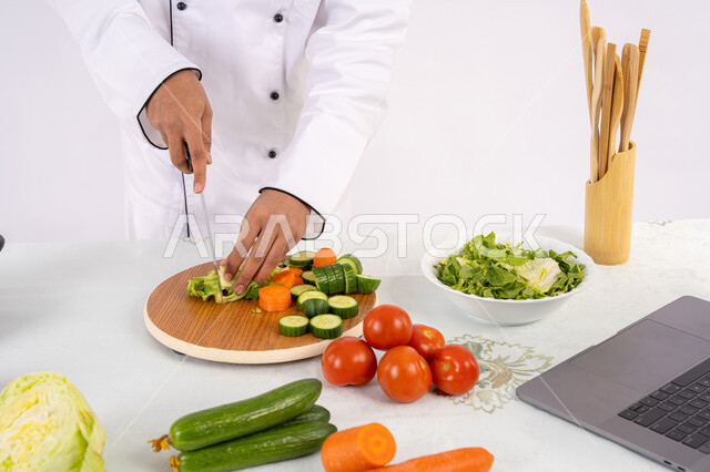 مهارة تقطيع الخضار، شغف التدرب على مهارة الطهي وإعداد الطعام، بورتريه مقرب لرجل عربي خليجي اماراتي يرتدي زي العمل يحضر طبق صحي مفيد، شيف سعودي يقوم بتحضير سلطة الخضراوات الطازجة، استخدام المكونات والمقادير المناسبة للوجبة، خلفية بيضاء