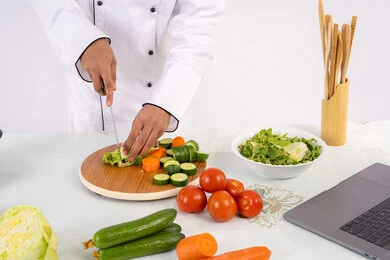 مهارة تقطيع الخضار، شغف التدرب على مهارة الطهي وإعداد الطعام، بورتريه مقرب لرجل عربي خليجي اماراتي يرتدي زي العمل يحضر طبق صحي مفيد، شيف سعودي يقوم بتحضير سلطة الخضراوات الطازجة، استخدام المكونات والمقادير المناسبة للوجبة، خلفية بيضاء