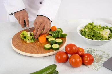 مفهوم مهنة طاهي الطعام، احترافية تقطيع الخضار، بورتريه مقرب لأيدي رجل عربي خليجي اماراتي يرتدي زي العمل يحضر طبق صحي مفيد، شيف سعودي يقوم بتحضير سلطة الخضراوات الطازجة، استخدام المكونات والمقادير المناسبة للوجبة، خلفية بيضاء