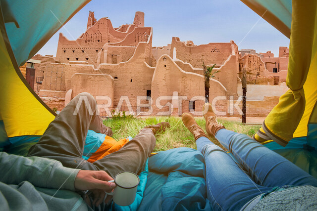 سائحان يجلسان داخل خيمة مطلة على حي الطريف التاريخي في الدرعية في المملكة العربية السعودية ، جمال وروعة المباني الاثرية والمعالم التاريخية في السعودية ، رحلة سياحية للاماكن التاريخية في السعودية