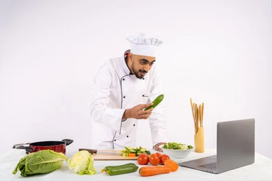تعلم وتطبيق فنون الطهي من خلال المواقع الإلكترونية باستخدام الحاسوب، توعية المجتمع بإعداد الطعام الصحي، بورتريه لرجل عربي خليجي اماراتي يرتدي زي العمل يقوم بتصوير وعرض الطبخ عبر اللابتوب، شيف سعودي يشرح المكونات والكميات المطلوبة عبر بث مباشر، خلفية بيضاء