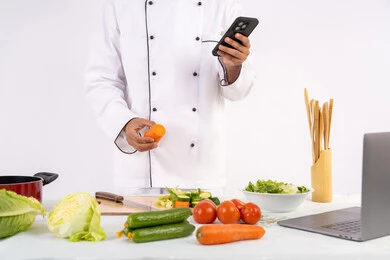 القيام بتوعية المجتمع بإعداد الطعام الصحي، تعلم وتطبيق فنون الطهي من خلال المواقع الإلكترونية عبر الحاسوب، بورتريه لرجل عربي خليجي اماراتي يرتدي زي العمل يقوم باستخدام الهاتف المحمول، شيف سعودي يحضر وصفة بالخضراوات الصحية، خلفية بيضاء