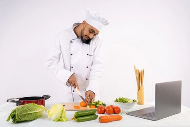 إجراء مكالمة هاتفية، التدرب على مهارة الطهي وإعداد الطعام عبر الحاسوب، بورتريه لرجل عربي خليجي اماراتي يرتدي زي العمل يقوم بتحضير وصفة طبق صحي مفيد من الانترنت، شيف سعودي يقوم بتقطيع الخضراوات الطازجة، استخدام المكونات والمقادير المناسبة للوجبة، خلفية بيضاء