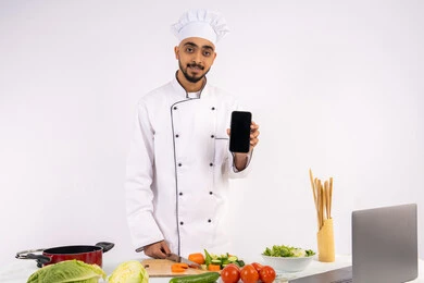 نشر الوعي في المجتمع بإعداد الطعام الصحي، تعلم وتطبيق فنون الطهي من خلال المواقع الإلكترونية باستخدام الحاسوب، بورتريه لرجل عربي خليجي اماراتي يرتدي زي العمل يقوم بعرض شاشة سوداء فارغة عبر الهاتف المحمول، شيف سعودي يحضر وصفة بالخضراوات الصحية، خلفية بيضاء