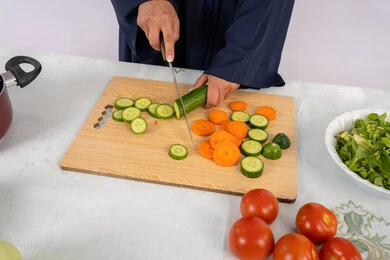 إعداد السلطات والاطباق الصحية، اتباع نظام غذائي صحي، شغف تعلم مهارة الطهي، بورتريه مقرب لسيدة عربية خليجية اماراتية ترتدي عباءة تقوم بتحضير طبق مفيد، ربة منزل سعودية تقوم بتقطيع الخضراوات الطازجة، خلفية بيضاء