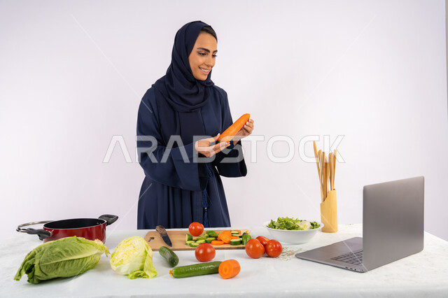 تعلم وتطبيق فنون الطهي من خلال المواقع الإلكترونية، توعية المجتمع بإعداد الطعام الصحي، بورتريه لامرأة عربية خليجية اماراتية محجبة ترتدي العباءة تقوم بتصوير وعرض الطبخ عبر اللابتوب، ربة منزل سعودية تشرح المكونات والكميات المطلوبة عبر بث مباشر، خلفية بيضاء