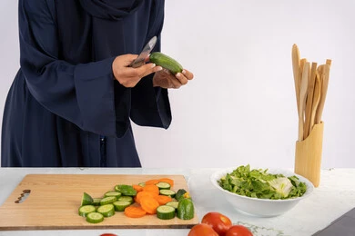 Learning cooking and food preparation skills via laptop, Saudi housewife preparing a recipe with fresh vegetables, professionalism in choosing vegetables, close-up portrait of a veiled Emirati Gulf Arab woman wearing an abaya preparing a healthy and useful meal, sharing recipes on websites, white background