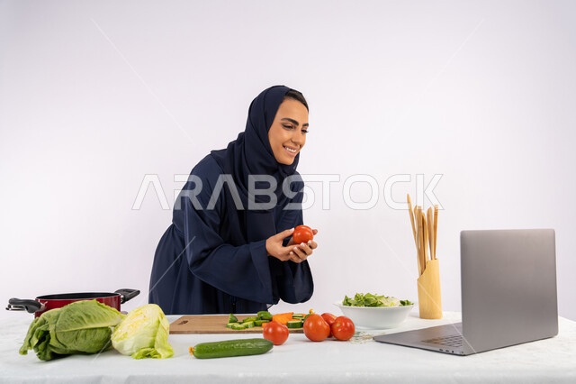 تعلم وتطبيق فنون الطهي من خلال المواقع الإلكترونية، توعية المجتمع بإعداد الطعام الصحي، بورتريه لامرأة عربية خليجية اماراتية محجبة ترتدي العباءة تقوم بتصوير وعرض الطبخ عبر اللابتوب، ربة منزل سعودية تشرح المكونات والكميات المطلوبة عبر بث مباشر، خلفية بيضاء