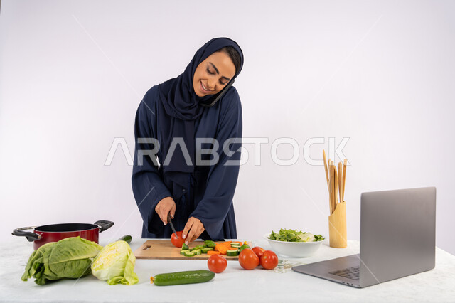 التحدث وإجراء مكالمة عبر الهاتف الجوال، إعداد السلطة الصحية، تعلم مهارة الطهي عبر الحاسوب، بورتريه لسيدة عربية خليجية اماراتية محجبة  ترتدي عباءة تقوم بتحضير وصفة طبق صحي مفيد من الانترنت، ربة منزل سعودية تقوم بتقطيع الخضراوات الطازجة، خلفية بيضاء
