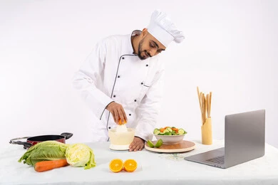 تصوير ومشاركة الوصفات على مواقع الانترنت، شيف سعودي يقوم بتحضير عصير مفيد، تعلم مهارة الطهي عبر الحاسوب المحمول، مفهوم النظام الغذائي الصحي، اعداد المشروبات الصحية والطازجة، بورتريه لرجل عربي خليجي اماراتي يرتدي زي الطهاة يعصر البرتقال الطازج، خلفية بيضاء