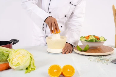 شيف سعودي يقوم بتحضير عصير مفيد، شغف تعلم مهارة الطهي، مفهوم النظام الغذائي الصحي، اعداد المشروبات الصحية والطازجة، بورتريه مقرب لرجل عربي خليجي اماراتي يرتدي زي الطهاة يعصر البرتقال الطازج، خلفية بيضاء