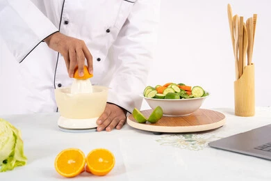 طباخ سعودي يقوم بتحضير عصير مفيد، شغف تعلم مهارة الطهي، مفهوم النظام الغذائي الصحي، اعداد المشروبات الصحية والطازجة، بورتريه مقرب لرجل عربي خليجي اماراتي يرتدي زي الطهاة يعصر البرتقال الطازج، خلفية بيضاء