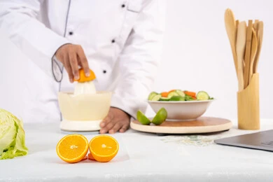 Healthy diet concept, Saudi chef preparing healthy juice, passion for learning cooking skill, preparing healthy and fresh drinks, close-up portrait of an Arab Gulf Emirati man wearing chef's uniform squeezing fresh oranges, white background