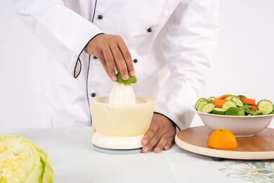 شيف سعودي يقوم بتحضير عصير مفيد، شغف تعلم مهارة الطهي، مفهوم النظام الغذائي الصحي، اعداد المشروبات الصحية والطازجة، بورتريه مقرب لرجل عربي خليجي اماراتي يرتدي زي الطهاة يعصر البرتقال الطازج، خلفية بيضاء