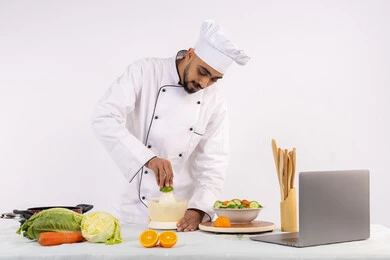 Enjoy photographing and sharing recipes on the Internet, a Saudi chef preparing a healthy juice, learning cooking skills via laptop, the concept of a healthy diet, preparing healthy and fresh drinks, a portrait of an Arab Gulf Emirati man wearing a chef's uniform squeezing fresh oranges, white background