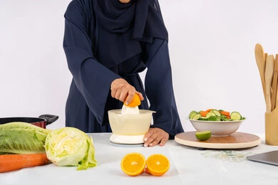 Having fun preparing delicious food, healthy diet concept, Saudi housewife preparing healthy juice, passion for learning cooking skill, preparing healthy and fresh drinks, close-up portrait of an Emirati Gulf Arab woman wearing an abaya squeezing fresh oranges, white background