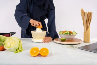 Diet and healthy eating, Saudi housewife preparing healthy juice, passion for learning cooking skills, preparing healthy and fresh drinks, close-up portrait of an Emirati Gulf Arab woman wearing an abaya squeezing fresh oranges, white background