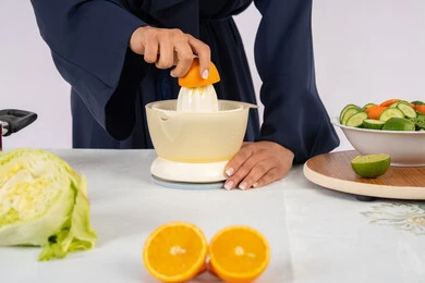 Healthy diet concept, Saudi housewife preparing healthy juice, passion for learning cooking skill, preparing healthy and fresh drinks, close-up portrait of an Emirati Gulf Arab woman wearing an abaya squeezing fresh oranges, white background