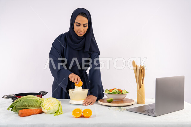 Sharing the recipe on social media, preparing healthy and fresh drinks, following a healthy diet, learning cooking skills using a computer, portrait of a veiled Emirati Gulf Arab woman wearing an abaya squeezing oranges, a Saudi housewife preparing a healthy dish, white background