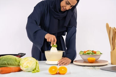 مفهوم النظام الغذائي الصحي، حب تعلم مهارة الطهي، اعداد المشروبات الصحية والطازجة، بورتريه لسيدة عربية خليجية اماراتية محجبة ترتدي عباءة تقوم بعصر الليمون الطازج، ربة منزل سعودية تقوم بتحضير عصير مفيد، خلفية بيضاء