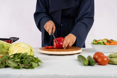 نمط ونظام غذائي صحي، إعداد السلطات والاطباق الصحية، شغف تعلم مهارة الطهي، بورتريه مقرب لسيدة عربية خليجية اماراتية ترتدي عباءة تقوم بتحضير طبق مفيد، ربة منزل سعودية تقوم بتقطيع الخضراوات الطازجة، خلفية بيضاء