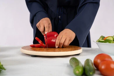 اتباع نظام غذائي صحي، إعداد السلطات والاطباق الصحية، شغف تعلم مهارة الطهي، بورتريه مقرب لسيدة عربية خليجية اماراتية ترتدي عباءة تقوم بتحضير طبق مفيد، ربة منزل سعودية تقوم بتقطيع الخضراوات الطازجة، خلفية بيضاء