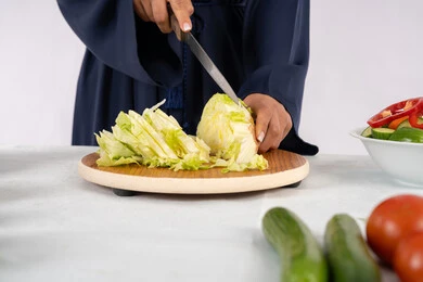 نمط ونظام غذائي صحي، إعداد السلطات والاطباق الصحية، شغف تعلم مهارة الطهي، بورتريه مقرب لسيدة عربية خليجية اماراتية ترتدي عباءة تقوم بتحضير طبق مفيد، ربة منزل سعودية تقوم بتقطيع الخضراوات الطازجة، خلفية بيضاء