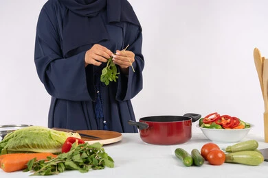 Saudi housewife preparing fresh vegetable salad, passion for practicing cooking and food preparation skills, professionalism in choosing vegetables, close-up portrait of an Emirati Gulf Arab woman wearing an abaya preparing a healthy and useful dish, white background