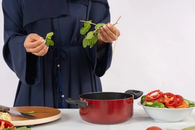 ربة منزل سعودية تقوم بتحضير سلطة الخضراوات الطازجة، شغف التدرب على مهارة الطهي وإعداد الطعام، احترافية اختيار الخضار، بورتريه مقرب لسيدة عربية خليجية اماراتية ترتدي عباءة تحضر طبق صحي مفيد، خلفية بيضاء