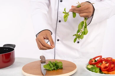 A Saudi chef preparing fresh vegetable salad, using appropriate ingredients and quantities for the meal, professionalism in choosing vegetables, passion for practicing cooking and food preparation skills, close-up portrait of an Emirati Gulf Arab man wearing work clothes preparing a healthy and useful dish, white background
