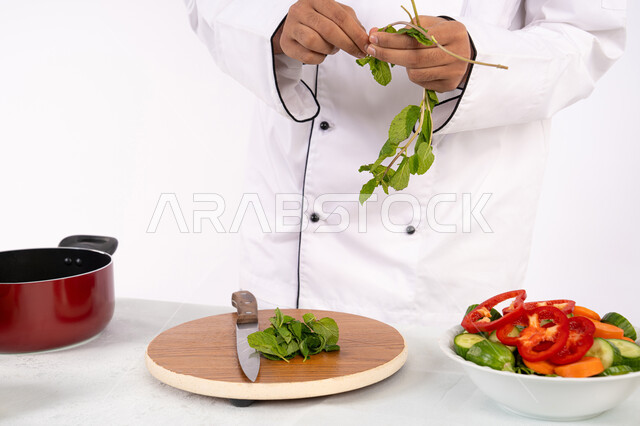 Passion for practicing cooking and food preparation skills, Saudi chef preparing fresh vegetable salad, using appropriate ingredients and quantities for the meal, professionalism in choosing vegetables, close-up portrait of an Arab Gulf Emirati man in work clothes preparing a healthy and useful dish, white background