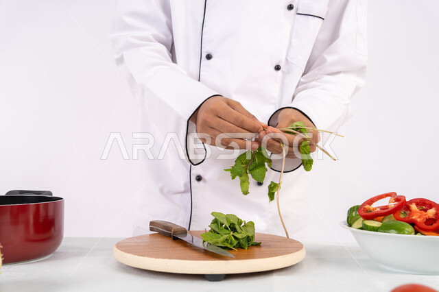 Saudi chef preparing fresh vegetable salad, using appropriate ingredients and quantities for the meal, professionalism in choosing vegetables, passion for practicing cooking and food preparation skills, close-up portrait of an Emirati Gulf Arab man wearing work clothes preparing a healthy and useful dish, white background