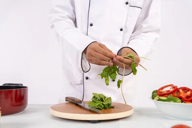 شيف سعودي يقوم بتحضير سلطة الخضراوات الطازجة، استخدام المكونات والمقادير المناسبة للوجبة، احترافية اختيار الخضار، شغف التدرب على مهارة الطهي وإعداد الطعام، بورتريه مقرب لرجل عربي خليجي اماراتي يرتدي زي العمل يحضر طبق صحي مفيد، خلفية بيضاء