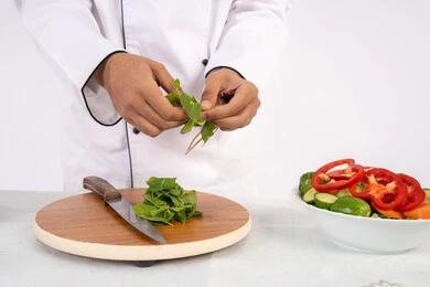 شيف سعودي يقوم بتحضير سلطة الخضراوات الطازجة، استخدام المكونات والمقادير المناسبة للوجبة، احترافية اختيار الخضار، شغف التدرب على مهارة الطهي وإعداد الطعام، بورتريه مقرب لرجل عربي خليجي اماراتي يرتدي زي العمل يحضر طبق صحي مفيد، خلفية بيضاء