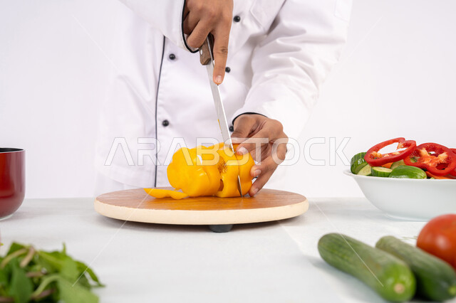 احترافية تقطيع الخضار، شغف التدرب على مهارة الطهي وإعداد الطعام، بورتريه مقرب لرجل عربي خليجي اماراتي يرتدي زي العمل يحضر طبق صحي مفيد، شيف سعودي يقوم بتحضير سلطة الخضراوات الطازجة، استخدام المكونات والمقادير المناسبة للوجبة، خلفية بيضاء
