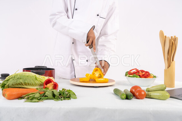 فن ومهارة تقطيع الخضار، شغف التدرب على مهارة الطهي وإعداد الطعام، بورتريه مقرب لرجل عربي خليجي اماراتي يرتدي زي العمل يحضر طبق صحي مفيد، شيف سعودي يقوم بتحضير سلطة الخضراوات الطازجة، استخدام المكونات والمقادير المناسبة للوجبة، خلفية بيضاء