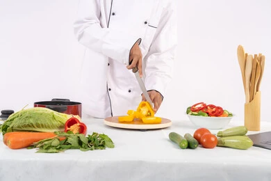 فن ومهارة تقطيع الخضار، شغف التدرب على مهارة الطهي وإعداد الطعام، بورتريه مقرب لرجل عربي خليجي اماراتي يرتدي زي العمل يحضر طبق صحي مفيد، شيف سعودي يقوم بتحضير سلطة الخضراوات الطازجة، استخدام المكونات والمقادير المناسبة للوجبة، خلفية بيضاء
