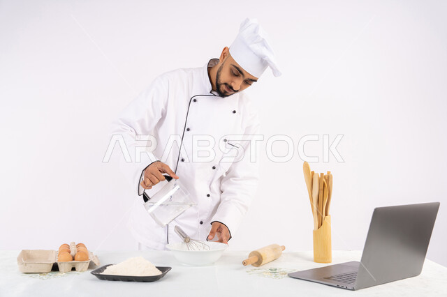 تصوير ومشاركة الوصفة عبر المواقع باستخدام الحاسوب المحمول، طاهي سعودي يقوم بتجهيز المكونات لصناعة الخبز والفطور، إعداد المخبوزات والمعجنات الشهية، بورتريه لرجل عربي خليجي اماراتي يرتدي زي العمل يقوم بخفق المكونات مع الدقيق الابيض لتحضير الطعام، خلفية بيضاء