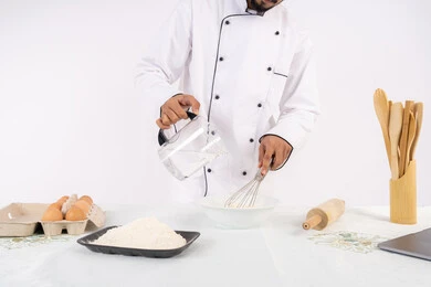 المخبوزات والمعجنات الشهية، بورتريه مقرب لرجل عربي خليجي اماراتي يرتدي زي العمل يقوم بخفق المكونات مع الدقيق الابيض لتحضير الطعام، شيف سعودي يقوم بتجهيز المكونات لصناعة الخبز والفطور، خلفية بيضاء