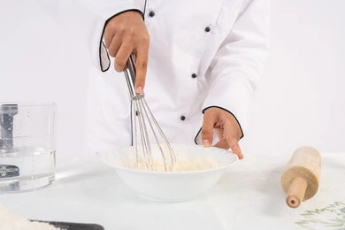 A Saudi chef prepares ingredients for making bread and breakfast, preparing delicious baked goods and pastries. A close-up portrait of an Emirati Gulf Arab man in work clothes mixing ingredients with white flour to prepare food, white background.
