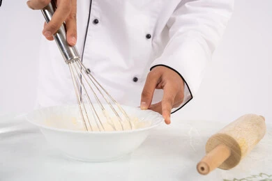 Preparing delicious baked goods and pastries. Close-up portrait of an Emirati Gulf Arab man in work clothes mixing ingredients with white flour to prepare food. A Saudi chef prepares ingredients for making bread and breakfast. White background.