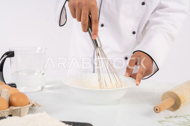 A Saudi chef prepares ingredients for making bread and breakfast, preparing delicious baked goods and pastries. A close-up portrait of an Emirati Gulf Arab man in work clothes mixing ingredients with white flour to prepare food, white background.