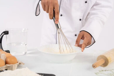 طاهي سعودي يقوم بتجهيز المكونات لصناعة الخبز والفطور، إعداد المخبوزات والمعجنات الشهية، بورتريه مقرب لرجل عربي خليجي اماراتي يرتدي زي العمل يقوم بخفق المكونات مع الدقيق الابيض لتحضير الطعام، خلفية بيضاء