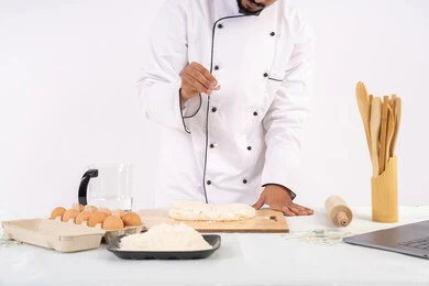 Photographing and sharing the recipe on social media using a laptop, a Saudi chef preparing ingredients for making bread and breakfast, preparing delicious baked goods and pastries, a portrait of an Emirati Gulf Arab man wearing work clothes mixing ingredients with white flour to preare food, white background