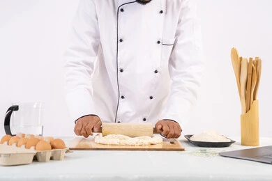 Sharing the recipe across websites using a laptop, preparing and baking delicious baked goods and pastries, portrait of an Emirati Gulf Arab man wearing work clothes rolling out dough using a rolling pin, a Saudi chef preparing ingredients for making bread and breakfast, white background
