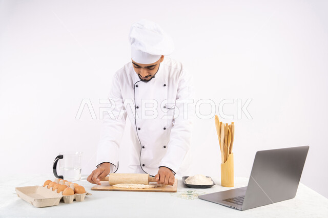 تصوير ومشاركة الوصفة عبر المواقع باستخدام الحاسوب المحمول، تحضير وإعداد المخبوزات والمعجنات الشهية، بورتريه لرجل عربي خليجي اماراتي يرتدي زي العمل يقوم بفرد العجين باستخدام الشوبك (النشابة)، شيف سعودي يقوم بتجهيز المكونات لصناعة الخبز والفطور، خلفية بيضاء