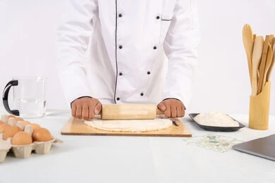 Preparing and preparing delicious baked goods and pastries, portrait of an Emirati Gulf Arab man wearing work clothes rolling out dough using a rolling pin, Saudi chef preparing ingredients for making bread and breakfast, white background